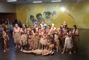Diversas fotos de pessoas vestidas com roupas indígenas, representando a encenação "Jabaquara... A terra de um sonho cidadão!", em um teatro com paredes amarelas.